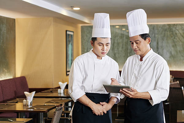 two chefs in uniform looking at a tablet